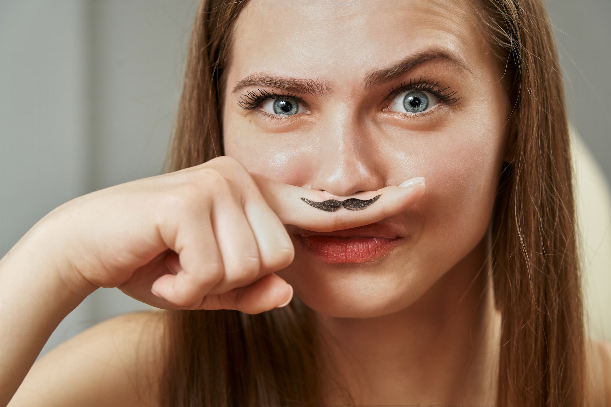 a funny young woman holds a finger near her nose, on which a black mustache is drawn. hormones