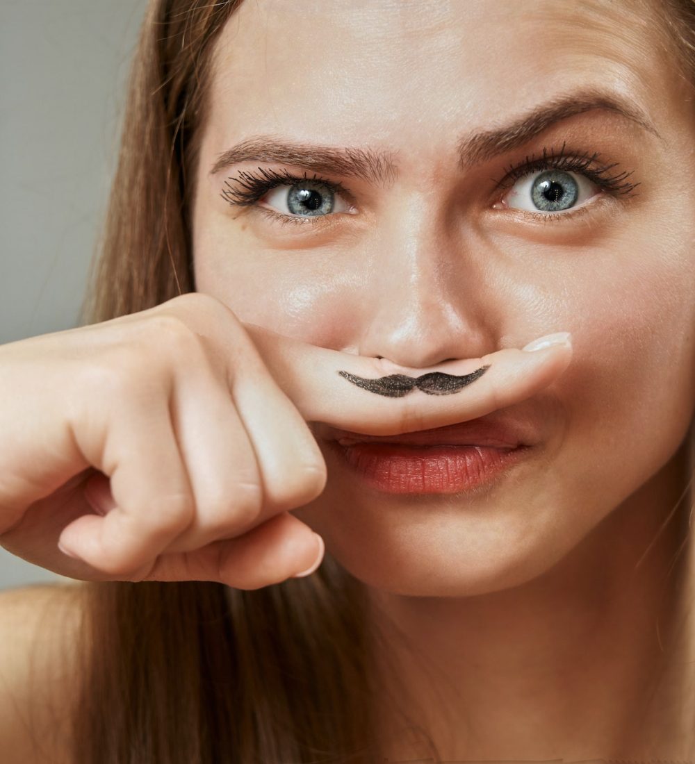 a funny young woman holds a finger near her nose, on which a black mustache is drawn. hormones