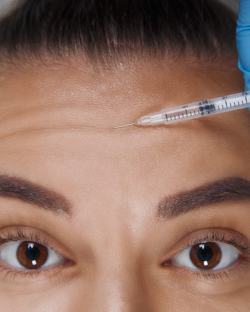 Cropped portrait of young Caucasian woman getting cosmetic injection of botox in forehead. People